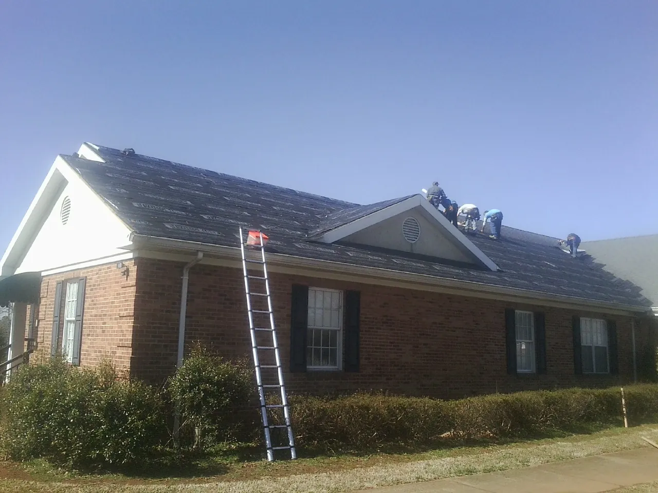 Crew tearing shingles off a brick ranch roof with a ladder set — Emergency Roof Repair work by our crew in Novato