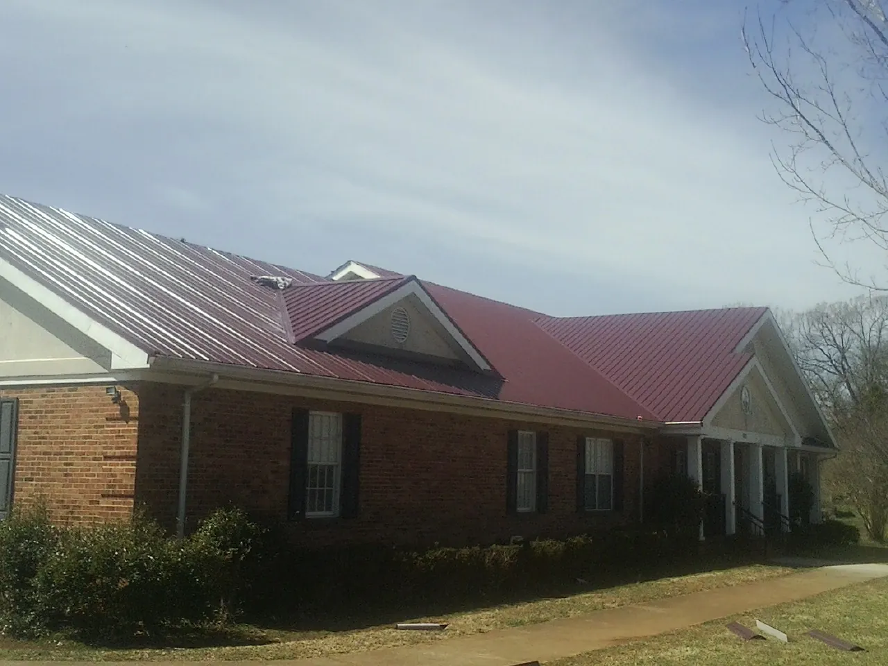 Red metal roof with gabled entries on a long brick building, from a Hail Damage Roof Repair job in Novato