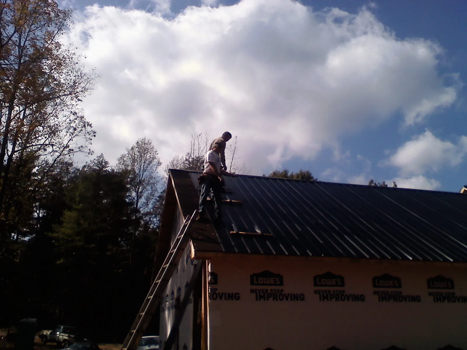 Roofer fastening dark metal panels high against a cloudy sky, from a Roof Inspection job in Novato