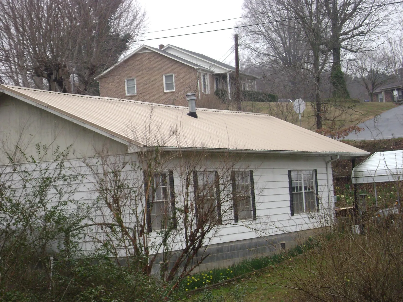 Tan metal roof on a white sided house set into a hillside — Commercial Roofing by Roofing Brothers in Novato